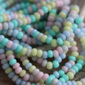 May include: A strand of pastel-colored glass beads in shades of light blue, pink, and green. The beads are small and round, and they are strung together on a clear thread.
