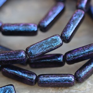 May include: A strand of dark blue and purple glass beads with a speckled finish. The beads are rectangular in shape and have a slightly iridescent sheen.