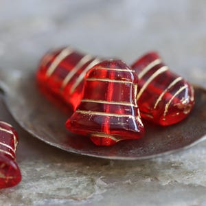 May include: Red glass Christmas bells with gold trim. The bells are on a silver spoon.