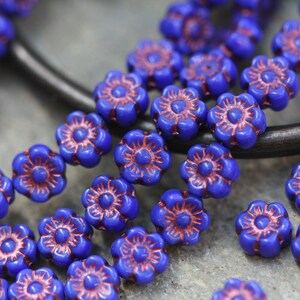May include: A strand of blue glass flower beads with a copper-colored center. The beads are strung on a wire and are arranged in a circular pattern.