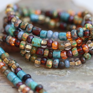May include: Multi-coloured beaded necklace with turquoise, brown, gold, and orange beads. The necklace is made of small, round beads and is layered in a decorative pattern.