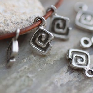 Puede incluir: Collar de plata con m&uacute;ltiples dijes de plata con un dise&ntilde;o en espiral. Los dijes est&aacute;n unidos a un cord&oacute;n de cuero marr&oacute;n.