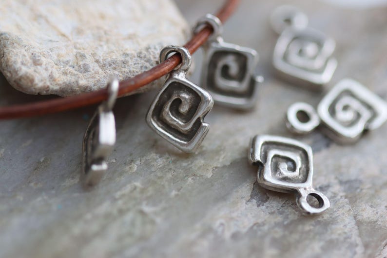 Puede incluir: Collar de plata con m&uacute;ltiples dijes de plata con un dise&ntilde;o en espiral. Los dijes est&aacute;n unidos a un cord&oacute;n de cuero marr&oacute;n.