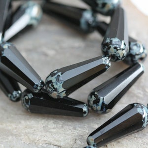 May include: A strand of black and white glass beads with a speckled pattern. The beads are shaped like teardrops and have a glossy finish.