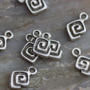 Puede incluir: Una colecci&oacute;n de dijes de metal plateado con un dise&ntilde;o en espiral. Cada dije tiene un bucle para sujetarlo a joyas u otras manualidades.