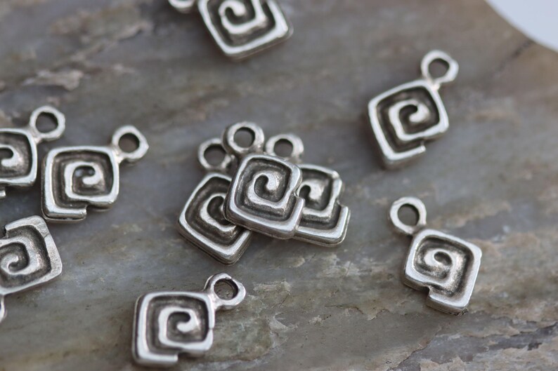 Puede incluir: Una colecci&oacute;n de dijes de metal plateado con un dise&ntilde;o en espiral. Cada dije tiene un bucle para sujetarlo a joyas u otras manualidades.
