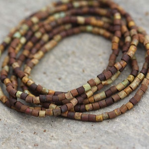May include: A strand of brown, green and beige ceramic beads. The beads are small and square-shaped.