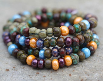 May include: A stack of colorful beaded bracelets in shades of brown, orange, blue, and purple. The beads are small and round, and they are arranged in a random pattern.