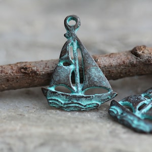 Puede incluir: Dos pequeños encantos de velero con un acabado de pátina turquesa. Los encantos están hechos de metal y tienen un diseño recortado.