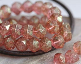 May include: A strand of pink iridescent glass beads with a faceted, star-shaped design. The beads are strung on a brown cord and are arranged in a circular pattern.