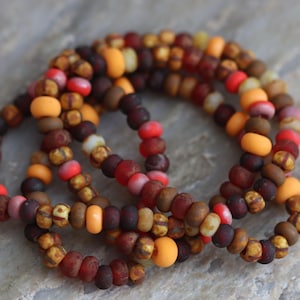 May include: A set of multi-coloured bracelets made with small glass beads in shades of brown, orange, red, and yellow.