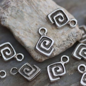 Puede incluir: Un grupo de dijes de metal plateado con un dise&ntilde;o en espiral. Cada dije tiene un bucle para sujetarlo a un collar, pulsera u otra joya.