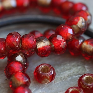 Può includere: Primo piano di perline di vetro rosso sfaccettate con accenti dorati. Le perline sono infilate insieme, mostrando il loro taglio intricato e le superfici riflettenti. Le perline sono probabilmente per la creazione di gioielli.