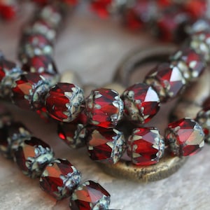 May include: A close-up of a strand of red glass beads with a metallic finish. The beads are faceted and have a vintage look.