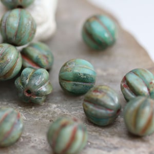 Peut inclure: Un ensemble de perles en verre vert et brun avec une surface texturée et côtelée. Les perles sont rondes et ont un aspect marbré.