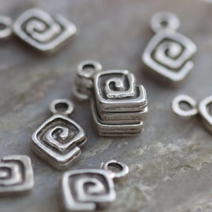 Puede incluir: Pendientes de amuleto de plata con un dise&ntilde;o en espiral. Los amuletos tienen forma cuadrada con esquinas redondeadas.