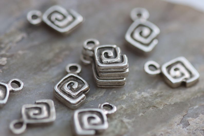 Puede incluir: Pendientes de amuleto de plata con un dise&ntilde;o en espiral. Los amuletos tienen forma cuadrada con esquinas redondeadas.