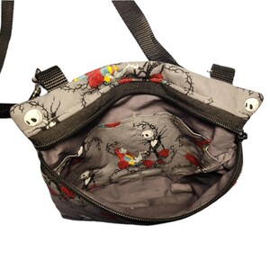 May include: A gray fabric crossbody bag with a black zipper and strap. The bag features a repeating pattern of Jack Skellington and Sally from the Nightmare Before Christmas.