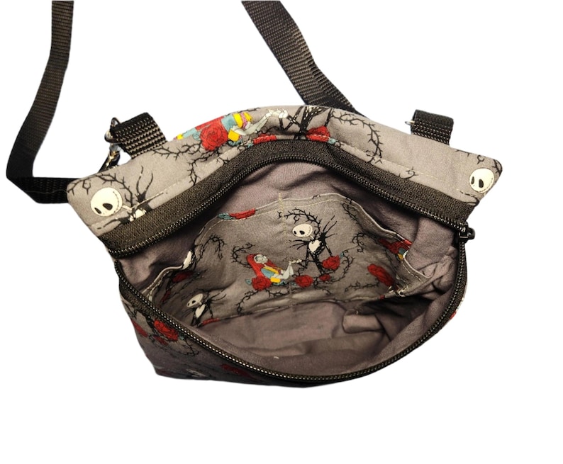 May include: A gray fabric crossbody bag with a black zipper and strap. The bag features a repeating pattern of Jack Skellington and Sally from the Nightmare Before Christmas.
