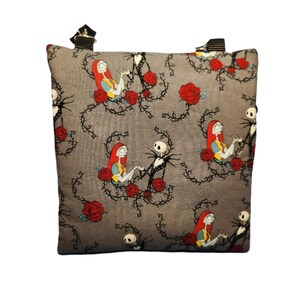 May include: A gray fabric tote bag with a repeating pattern of Jack Skellington and Sally from The Nightmare Before Christmas. The pattern features the characters holding hands and surrounded by red roses and thorns.