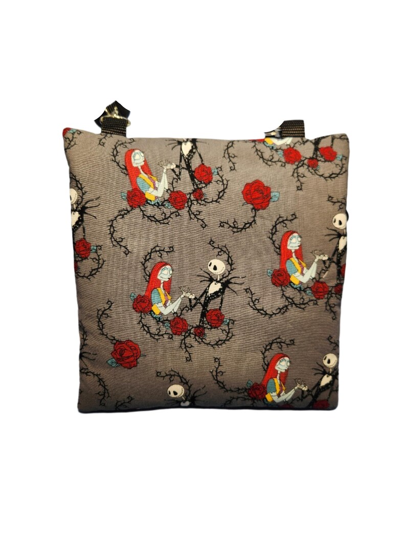 May include: A gray fabric tote bag with a repeating pattern of Jack Skellington and Sally from The Nightmare Before Christmas. The pattern features the characters holding hands and surrounded by red roses and thorns.