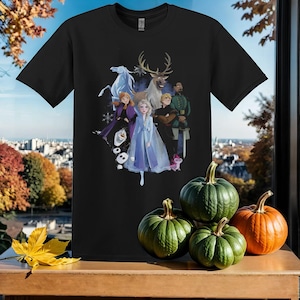 Puede incluir: Camiseta negra con un estampado gráfico de personajes de la película animada Frozen. Los personajes incluyen a Elsa, Anna, Kristoff, Sven y Olaf. La camiseta es un gran regalo para los fans de la película.