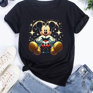 以下が含まれることがあります： 星形のハート型の輪郭を持つ座っているミッキーマウスのグラフィックプリントが施された黒いTシャツ。