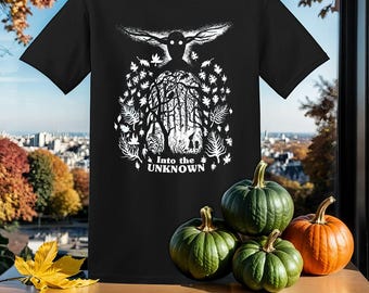 Peut inclure: T-shirt noir avec un motif blanc d'une créature aux ailes déployées et le texte "Into the Unknown". Le motif est entouré de feuilles et d'arbres.