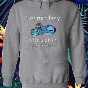 Puede incluir: Sudadera gris con capucha con un personaje azul Stitch de Lilo & Stitch. El texto en la sudadera dice "No soy perezoso, solo estoy en modo de ahorro de energ&iacute;a."