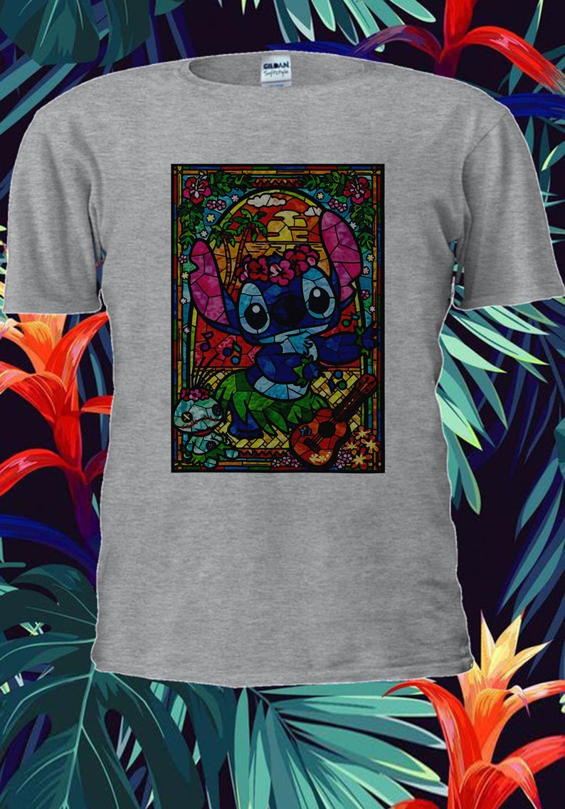 Pu&ograve; includere: Una maglietta grigia con un'immagine di Stitch di Lilo & Stitch in stile vetrata. Stitch sta suonando un ukulele e indossa una collana di fiori. L'immagine &egrave; circondata da una cornice colorata.