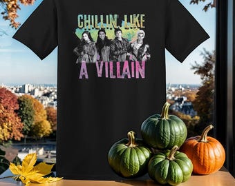 May include: Black t-shirt featuring a graphic of four people standing together. The text "Chillin' Like A Villain" is printed in pink and blue on the shirt.