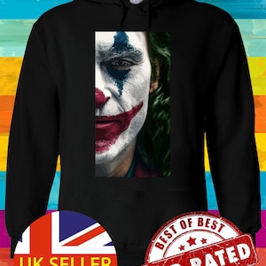 May include: Black hooded sweatshirt featuring a close-up of the Joker's face, with white face paint, red lips, and blue eye makeup. The sweatshirt has a drawstring hood and a kangaroo pocket. The image is centered on the chest.