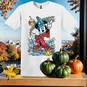 May include: White t-shirt featuring a colourful illustration of Mickey Mouse dressed as a wizard. Mickey is holding a wand and is surrounded by stars and magic.