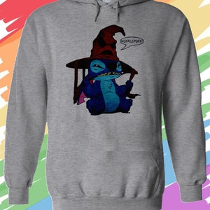 May include: A gray hooded sweatshirt with a blue Stitch character wearing a red and black wizard hat. The hat has a pointed top and a wide brim. The character is holding a wand in its right hand and has a speech bubble above its head that says "Hufflepuff!"