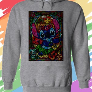 Puede incluir: Una sudadera con capucha gris con una imagen de Stitch de Lilo & Stitch tocando el ukelele en estilo vitral. La imagen est&aacute; rodeada por un borde colorido con flores y palmeras.