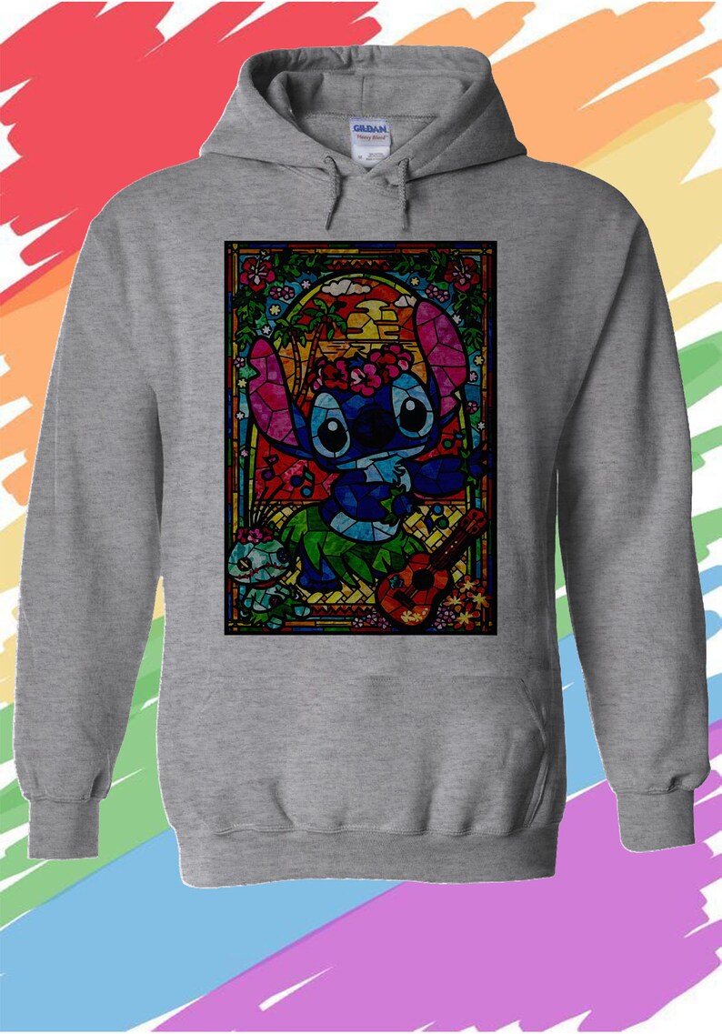 Puede incluir: Una sudadera con capucha gris con una imagen de Stitch de Lilo & Stitch tocando el ukelele en estilo vitral. La imagen est&aacute; rodeada por un borde colorido con flores y palmeras.