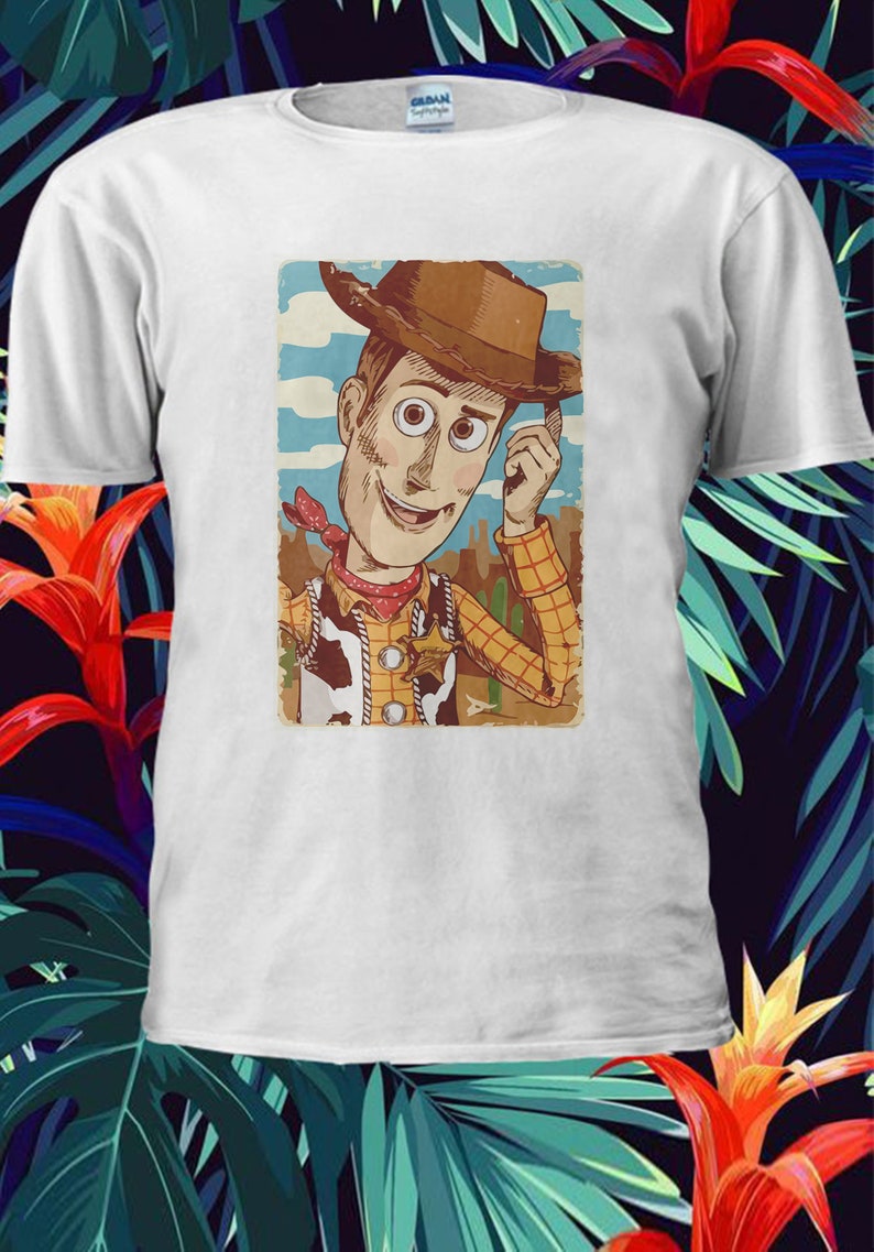 以下が含まれることがあります： トイストーリーのウッディのヴィンテージスタイルのイラストが描かれた白いTシャツ。ウッディはトレードマークのテンガロンハットとベストを着て、笑顔を見せています。イラストは茶色の枠で囲まれています。