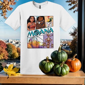 May include: White t-shirt with a colorful graphic print featuring characters from the animated movie Moana. The graphic includes Moana, Maui, a pig, a rooster, and a crab. The text "Moana" is printed in blue letters.