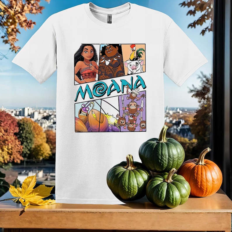 May include: White t-shirt with a colorful graphic print featuring characters from the animated movie Moana. The graphic includes Moana, Maui, a pig, a rooster, and a crab. The text "Moana" is printed in blue letters.