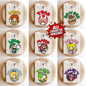 May include: Nine cream-coloured t-shirts featuring various characters from the Mario video game series. Each shirt displays a different character's image and name in a colourful, circular design. The text "ALL CHARACTER AVAILABLE" is also visible.