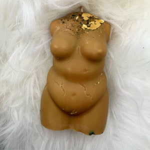 Könnte beinhalten: Eine braune, handgefertigte Kerze in Form eines menschlichen Torsos. Die Kerze hat eine strukturierte Oberfläche und ist mit goldenen Flocken verziert.