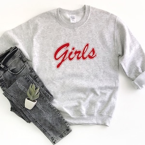 以下が含まれることがあります： グレーのトレーナーに赤い文字で「Girls」と書かれている