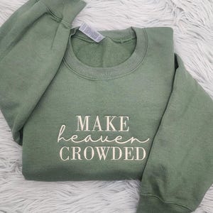 May include: A green sweatshirt with the text "MAKE heaven CROWDED" printed in white on the front.