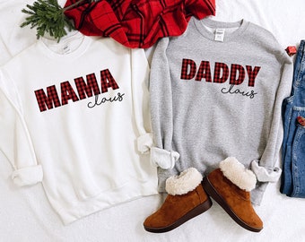 May include: Two white and grey sweatshirts with red and black buffalo plaid lettering. The white sweatshirt says "Mama Claus" and the grey sweatshirt says "Daddy Claus".