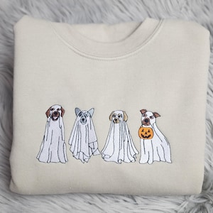 May include: A beige sweatshirt with an embroidered design of four dogs dressed as ghosts for Halloween. Three of the dogs are wearing white ghost costumes, and one dog is holding a small orange pumpkin.