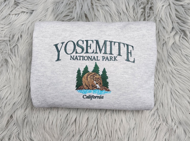 May include: A gray sweatshirt with an embroidered design featuring the words "Yosemite National Park" and a bear in a forest setting. The text "California" is also embroidered below the bear.