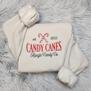 Sudadera navideña de Kringle Candy Co. con cuello redondo y bastones de caramelo bordados