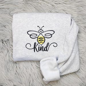 May include: A gray sweatshirt with a black and yellow bee design and the word "Kind" in a cursive font.