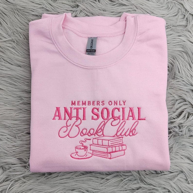 May include: Pink sweatshirt with the text "Members Only Anti Social Book Club" embroidered in pink. The design includes a cup of coffee and a stack of books.
