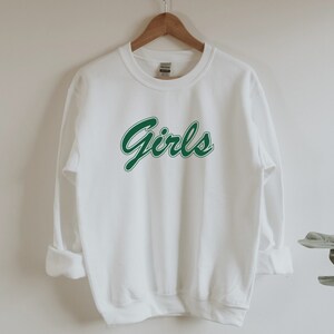 以下が含まれることがあります： 前面に緑色の「Girls」のグラフィックがプリントされた白いスウェットシャツ